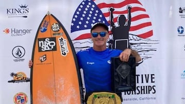 El surfista de Zarautz Aitor Francesena muestra el trofeo y el cintur&oacute;n de campe&oacute;n del US Open, sujetando su tabla de surf con la mano y con un photocall detr&aacute;s del campeonato. 