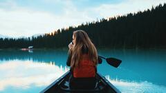 Mujer en Kayak por un lago con los árboles y el cielo reflejados en el agua.