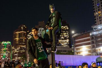 Aficionado de los Celtics con gorro de Batman celtic, subido a una señal de tráfico.
