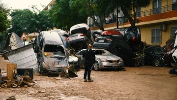 Un hombre observa montones de automóviles arrastrados por las recientes inundaciones repentinas en el cercano municipio de Alfafar.