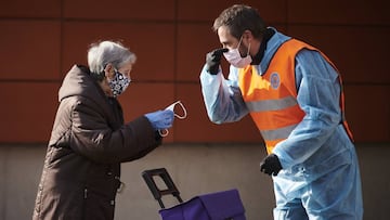Un trabajador de Protección Civil entrega una mascarilla a una mujer mientras le explica cómo ponérsela.