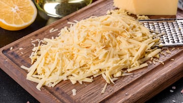 Fresh hard cheese grated on a large grater on a wooden cutting board on a dark concrete background