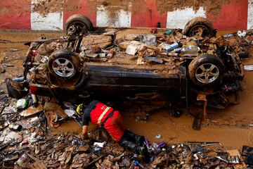 Un bombero busca víctimas en un coche averiado tras las fuertes lluvias que provocaron inundaciones en Alfafar, cerca de Valencia.