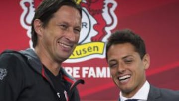 El delantero mexicano sonr&iacute;e junto al entrenador del Bayern Leverkusen, Roger Schmidt, durante una rueda de prensa en el BayArena en Leverkusen. 