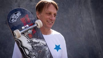 Tony Hawk con una camiseta blanca sonriendo y con una tabla de skate de Birdhoue agarrada. 