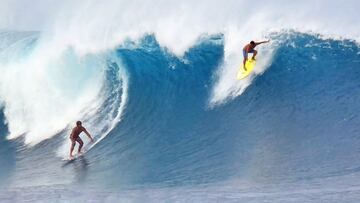 Un surfista en el bottom de la ola de Banzai Pipeline (Oahu, Hawái) y otro realizando el drop desde el labio justo delante suyo. Ambos en bañador, en un swell XXL de este mes de febrero del 2021.