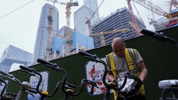 FILE PHOTO: A worker puts on a cooling seat cover on a bicycle of a bike-sharing service in Beijing's Central Business District (CBD), China July 14, 2024. REUTERS/Tingshu Wang/File Photo