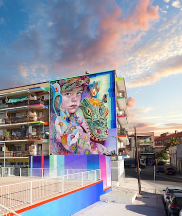 
En Fuenlabrada, una ráfaga de rosas, turquesas y verdes abraza la fachada. La niña con el cocodrilo convierte la esquina en un icono tierno y luminoso que irradia fantasía.