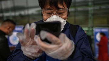 Un habitante de Wuhan, provisto con mascarilla, consulta su tel&eacute;fono m&oacute;vil.