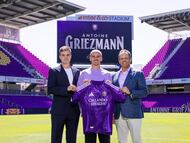 USA9339. ORLANDO (FL, EEUU), 24/03/2026.- Fotografía cedida por el Orlando City SC que muestra al futbolista francés Antoine Griezmann (c) sosteniendo la camisa del club junto a su propietario y presidente, Mark Wilf (d), y su director general y deportivo, Ricardo Moreira (i), este lunes en Orlando, Florida. El delantero Antoine Griezmann, máximo goleador de la historia del Atlético de Madrid, cerró este martes su fichaje por el Orlando City, con el que ha firmado por dos años más un tercero opcional y al que se incorporará a partir de la próxima temporada, en julio de 2026, una vez finalice el presente curso con el conjunto rojiblanco, según anunciaron ambos clubes en sendos comunicados. EFE/Mark Thor/Orlando City SC /- SOLO USO EDITORIAL/SOLO DISPONIBLE PARA ILUSTRAR LA NOTICIA QUE ACOMPAÑA (CRÉDITO OBLIGATORIO) -