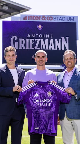 USA9339. ORLANDO (FL, EEUU), 24/03/2026.- Fotografía cedida por el Orlando City SC que muestra al futbolista francés Antoine Griezmann (c) sosteniendo la camisa del club junto a su propietario y presidente, Mark Wilf (d), y su director general y deportivo, Ricardo Moreira (i), este lunes en Orlando, Florida. El delantero Antoine Griezmann, máximo goleador de la historia del Atlético de Madrid, cerró este martes su fichaje por el Orlando City, con el que ha firmado por dos años más un tercero opcional y al que se incorporará a partir de la próxima temporada, en julio de 2026, una vez finalice el presente curso con el conjunto rojiblanco, según anunciaron ambos clubes en sendos comunicados. EFE/Mark Thor/Orlando City SC /- SOLO USO EDITORIAL/SOLO DISPONIBLE PARA ILUSTRAR LA NOTICIA QUE ACOMPAÑA (CRÉDITO OBLIGATORIO) -