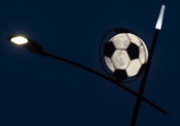 La luna brilla detrás de una farola decorada con la silueta de un balón de fútbol.
