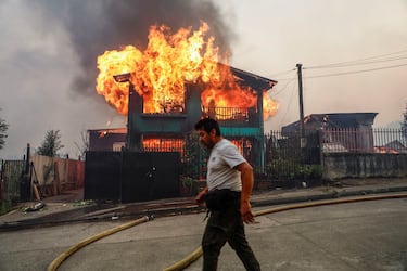 Una persona camina frente a un edificio en llamas mientras el fuego y el humo se elevan de un incendio forestal en la región del Biobío, donde, según medios locales, múltiples incendios forestales provocaron evacuaciones de emergencia, en Concepción, Chile.