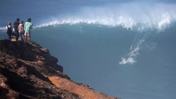Una familia observa desde el acantilado de Nazar&eacute; a un surfista surfeando una ola gigante en Praia do Norte. 