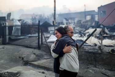 La gente se abraza frente a edificios quemados mientras el fuego y el humo se elevan de un incendio forestal en la región del Biobío, donde, según medios locales, múltiples incendios forestales provocaron evacuaciones de emergencia, en Concepción, Chile.