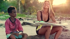 Surfista francesa Maud Le Car en bikini negro y con su tabla de surf en las Mentawai, sentada al lado de un ni&ntilde;o local. 