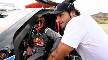 Ferrari's Spanish Formula One driver Carlos Sainz Jr (R), son of rally driver Carlos Sainz (L), speaks with his father by his vehicle before the start of the second stage of the Dakar 2023 rally between Sea Camp and al-Ula in Saudi Arabia on January 2, 2023. (Photo by FRANCK FIFE / AFP)