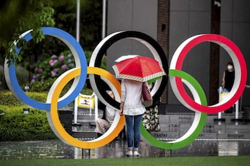 Una viandante se fotografía bajo la lluvia junto a los aros olímpicos que lucen en Tokio muy cerca del Estadio Nacional. La capital japonesa acoge la ceremonia de inauguración de unos Juegos a los que la pandemia ha rodeado de dudas e incertidumbre, y que ya obligó a retrasarlos un año. 