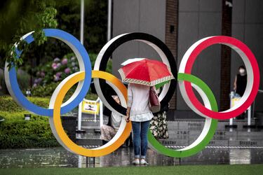 Una viandante se fotografía bajo la lluvia junto a los aros olímpicos que lucen en Tokio muy cerca del Estadio Nacional. La capital japonesa acoge la ceremonia de inauguración de unos Juegos a los que la pandemia ha rodeado de dudas e incertidumbre, y que ya obligó a retrasarlos un año. 