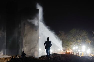 Un chorro de agua se rocía sobre un edificio mientras el personal de seguridad se encuentra en el lugar del accidente después de que un avión de Air India, con destino al aeropuerto Gatwick de Londres, se estrellara durante el despegue de un aeropuerto en Ahmedabad, India.