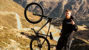 El piloto de MTB Jake100 posa con su bici de montaña mientras hace el signo de los cuernos frente a la carretera en la que consigue llegar a los 100 kilómetros por hora de wheeelie.
