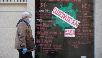 Un hombre con mascarilla y guantes pasa al lado de un escaparate de una tienda con el mensaje de &ldquo;Qu&eacute;date en casa&rdquo;