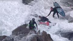 Dos miembros del equipo de rescate de la Polic&iacute;a de Nueva Zelanda en el rescate a un surfista entre las rocas de una playa de arena negra. 