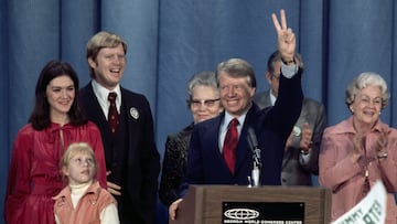 11/3/1976-Atlanta, GA- Jimmy Carter using the southland as a base put together a coalition of big-city voters and blacks and defeated President Ford by getting 272 electoral votes.-- Photo depicts Carter with family and supporters behind a podium waving the victory sign. Carter's 9-year-old daughter Amy is on his right, as well as John and Judy Carter.