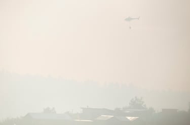 Un helicóptero de extinción de incendios vuela en medio del humo tras la propagación de incendios forestales, en Viña del Mar, Chile.