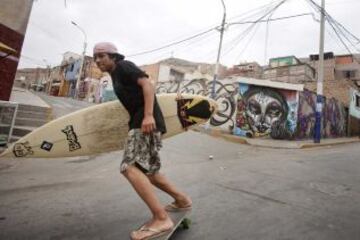 Un joven en un monopatín se dirige a sus clases de surf en una playa cerca de Alto Perú barrio de chabolas de Lima. Desde 2008, la ONG Alto Perú busca ofrecer a los niños de un barrio pobre de pescadores conocido como Alto Perú, la oportunidad de aprender y practicar deportes alternativos como el surf y el Muay Thai de forma gratuita.