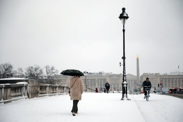 Una mujer camina con un paraguas sobre el Puente de la Concordia cubierto de nieve en París.