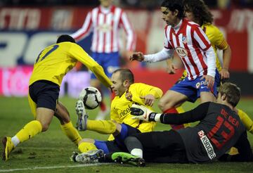 El jugador del Barcelona Iniesta trata de controlar el balón desde el suelo ante el portero del Atlético De Gea. 
