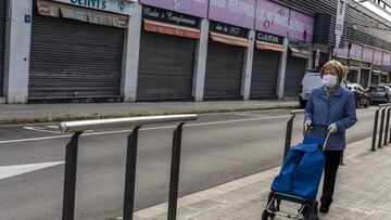 Una mujer camina por la calle para ir a comprar y lleva mascarilla.