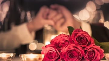 Pareja tomada de la mano sobre una mesa con rosas vía Getty Images.
