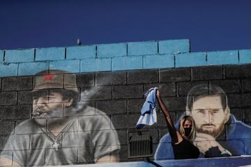 A woman reacts in front of a mural depicting the late soccer legend Diego Armando Maradona and soccer player Lionel Messi near Bella Vista cemetery, on the outskirts of Buenos Aires, Argentina