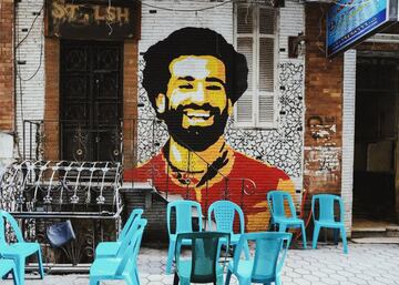 Tambi¨¦n Mohamed Salah trasciende fronteras. La estrella del Liverpool ha sido galardonado por la Asociaci¨®n de F¨²tbol de Egipto, tras convertirse en el primer jugador de ese pa¨ªs que gana la Premier y la Champions. Adem¨¢s del reconocimiento deportivo, el delantero ha conseguido el cari?o y la admiraci¨®n de sus compatriotas. Se palpa paseando por el centro de El Cairo. Su amplia sonrisa sirve como reclamo a un caf¨¦ y da la bienvenida a la ¡®Escuela Industrial Mohamed Salah¡¯ en Gharbiya. Encabeza un grupo de internacionales de su selecci¨®n, en el graffiti de un paso subterr¨¢neo que conecta la isla de Zamalek con el centro. Salah es un ¨ªdolo en su lugar de origen y de destino. En Liverpool acompa?aron su rostro con un poema y ha conquistado la fachada de un edificio en Times Square (Nueva York), gracias al artista Brandan ¡®bmike¡¯ Odums. Se hizo viral cuando el futbolista lo tuite¨®.