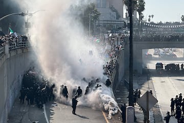 Agentes de policía están envueltos en una nube de humo de gases lacrimógenos y granadas de percusión mientras custodian una rampa de entrada a una autopista durante una protesta contra las redadas federales de inmigración en el centro de Los Ángeles.