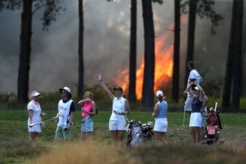 Las jugadoras de golf, Sophie Powell, Cara Gainer y Gabriella Cowley y sus caddies miran como un incendio se acerca a ellas durante la Rose Ladies Series en Virginia Water, Inglaterra.