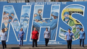 NHS workers stand in front of a mural painted in recognition of the NHS on the Falls Road.