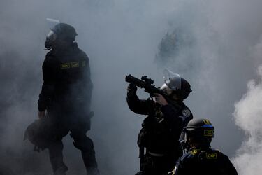 Un agente de policía apunta con un arma en medio del humo durante una protesta contra las redadas federales de inmigración en el centro de Los Ángeles.