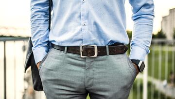 An unrecognizable young businessman with a bag and a leather belt walking on a bridge, hands in pockets.