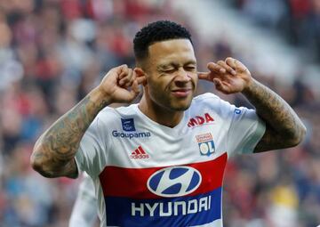 Lyon's Memphis Depay celebrates scoring their first goal with his fingers in his ears.