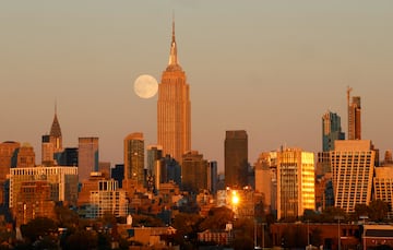 La superluna del cazador se alza detrás del horizonte del centro de Manhattan y el Empire State Building en la ciudad de Nueva York mientras se pone el sol el 16 de octubre de 2024, visto desde Jersey City, Nueva Jersey.