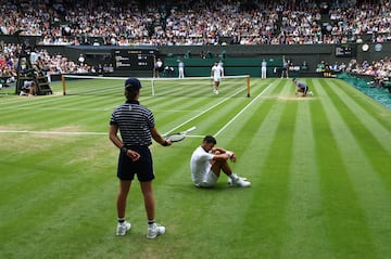 Una recogepelotas sostiene la raqueta de Novak Djokovic ofreciéndosela al tenista serbio para que siga jugando el partido cuando se levante del suelo.