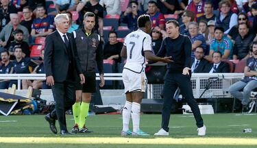 El entrenador del Barcelona, Xavi Hernández, habla con el jugador del Real Madrid, Vinicius, en la banda durante el partido ante la mirada de Carlo Ancelotti. 