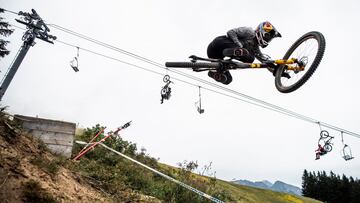 Finn Iles saltando con su bici en la UCI MTB DH World Cup en el BIke Park de Les Gets, Francia. Con un telesilla con varios riders y sus bicis todoterreno al fondo. 