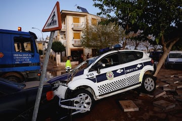 Un vehículo policial averiado yace atrapado entre un coche y un árbol tras las inundaciones en Utiel, España.