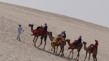 People ride camels on the dunes in Al Wakrah, south of Doha, on December 12, 2022, during the Qatar 2022 World Cup football tournament. (Photo by David GANNON / AFP)