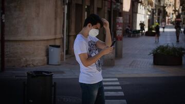 Un joven con mascarilla camina mirando el m&oacute;vil.