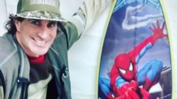 El surfista Carlitos Di Pace sonriendo, con gorra, mostrando una tabla de surf de su hijo pintada con un dibujo de Spiderman.